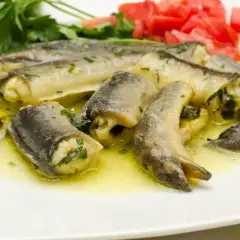Délicieux morceaux d'anguille roulée, baignant dans une sauce dorée, parfaits pour apprendre comment préparer une anguille. Garniture de persil et tomates.