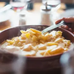 Une main saisit une fourchette pour déguster une généreuse portion de la patia crémeuse, un plat réconfortant servi dans un bol en terre cuite.