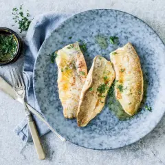 Trois filets de féra au four, parsemés de persil frais, sur une assiette bleue. Une petite coupelle de sauce et des couverts complètent cette recette simple.