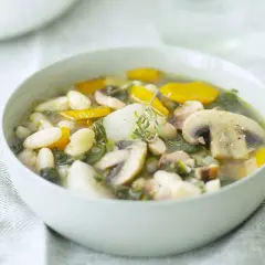 Un bol de soupe haricots blancs réconfortante avec des champignons, des carottes et des herbes fraîches.