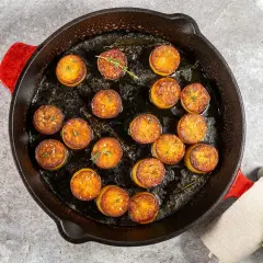 Pommes de terre en sauce brune, dorées et savoureuses, mijotent dans une poêle en fonte avec des herbes aromatiques.
