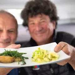 Deux hommes souriants présentent une assiette avec des ormeaux et des légumes. Une recette d'ormeau digne d'un grand chef.