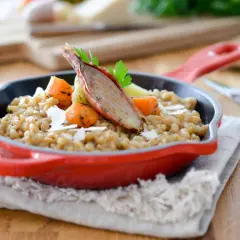 Un savoureux risotto d'épeautre garni de carottes rôties et d'une échalote confite, servi dans une cocotte rouge.