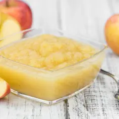 Un bol de compote pommes poires maison, avec des pommes fraîches coupées en arrière-plan.
