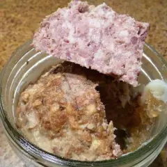 Un bocal de marmiton pâté de sanglier en bocaux stérilisés, avec une tranche de pâté posée sur le bord.
