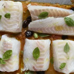 Cinq pavés de dos de cabillaud à la provençale au four, baignant dans une sauce tomate et olives, ornés de feuilles de basilic frais.