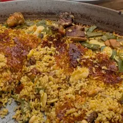 Gros plan sur une paella au feu de bois, avec du riz doré, des haricots verts, des morceaux de viande et une croûte croustillante.