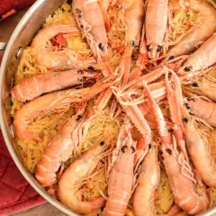 Un plat de fideuà catalana, avec des pâtes fines et des crevettes roses généreuses, prêt à être dégusté.