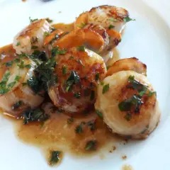 Délicieuse poêlée du pêcheur : Saint-Jacques poêlées, dorées et nappées d'une sauce savoureuse, parsemées de persil frais.