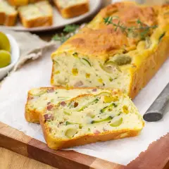 Savoureux cake salé aux courgettes et olives, parfait pour une recette d'oreille d'ours. Servi tranché sur une planche en bois.
