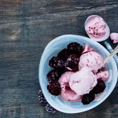 Délicieuse recette de glace avec fruits congelés et yaourt, garnie de mûres fraîches. Une cuillère sert la glace rose crémeuse.