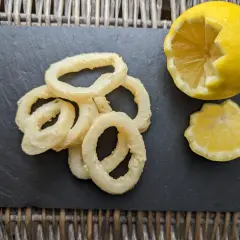 Anneaux de calamar à l'andalouse dorés et croustillants, servis avec un quartier de citron sur une ardoise.