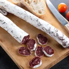 Deux saucissons secs, dont un tranché, sur une planche en bois avec du pain et des tomates cerises. Un délice de saucisson au genévrier.