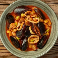 Zarzuela la vraie recette espagnole : un plat de fruits de mer savoureux avec des moules, des calamars et des légumes dans une sauce rouge.