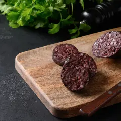 Tranché sur une planche en bois, un boudin noir froid révèle sa texture riche. Du persil frais et un moulin à poivre complètent la scène.