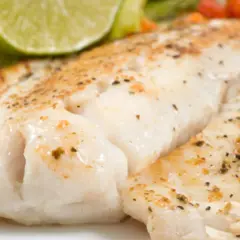 Filet de turbot au four en papillote, tendre et savoureux, servi avec une tranche de citron vert et des légumes croquants.