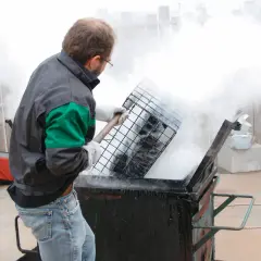 Un homme en tenue de travail manipule une grille au-dessus d'un récipient fumant, peut-être pour un gigot bitume.