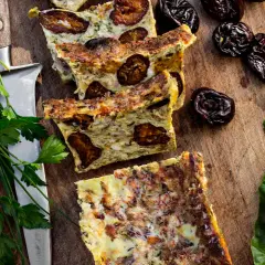 Tranches de **punti salé** aux pruneaux, sur une planche en bois, avec des herbes fraîches et des feuilles vertes.