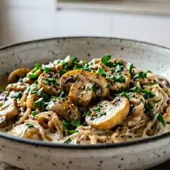 Un plat de champignons à la crème, parsemé de persil frais et de poivre noir. Une délicieuse recette oronges à la crème.