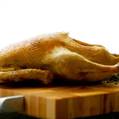 Canard entier doré, prêt pour une recette tanche entière au four. Sur une planche en bois, avec des herbes.