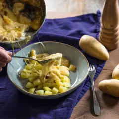 Une cuillère sert du fromage fondu sur des pommes de terre coupées, rappelant la saveur authentique de la matouille origine.