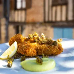 Un plat de ris de veau meunière croustillant, garni de câpres et servi avec un quartier de citron et une sauce verte.