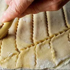 Main d'une personne utilisant une roulette pour découper une pâte à gâteau en losanges.