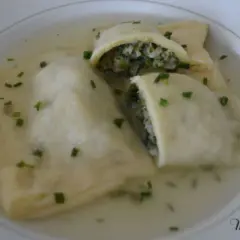 Trois maultaschen à la poêle, généreusement garnies de légumes verts et de viande, baignent dans un bouillon clair, parsemé de ciboule fraîche.