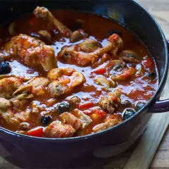 Un plat mijoté de râble de lapin à la provençale, avec des olives noires et des champignons, dans une cocotte en fonte.