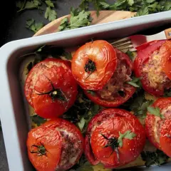 Tomates farcies à la viande dans un plat, prêtes pour le temps de cuisson. Garnies de persil frais.
