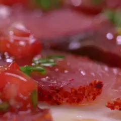Carpaccio de bonite, fines tranches de poisson cru garnies de dés de tomates rouges et d'herbes vertes, assaisonné d'épices.