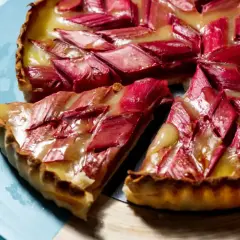 Tarte rhubarbe/pommes crémeuse aux éclats rouges et dorés, une part coupée sur une assiette bleue.