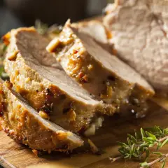 Tranches de porc rôti, parfaites pour le temps de cuisson cochon de lait au barbecue. Garnies d'herbes fraîches sur une planche en bois.
