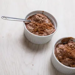 Deux ramequins de mousse au chocolat en poudre, l'un avec une cuillère, sur une table en bois clair.