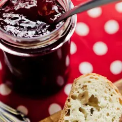 Un pot de confiture sombre, peut-être d'origine confiture de vieux garçon, sur une nappe à pois rouges. Du pain frais est prêt à être tartiné.
