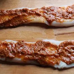 Deux filets de poisson blanc crus, recouverts d'une sauce rouge épicée, sur une planche à découper en bois.