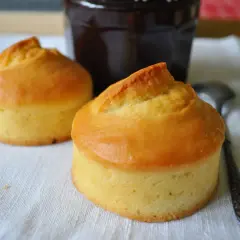Deux petits gâteaux dorés, rappelant les vieilles recettes de gâteau à la peau de lait, sont prêts à être dégustés avec un pot de confiture sombre.