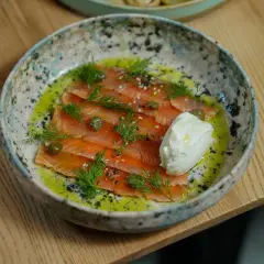 Saumon gravlax maison, fines tranches de poisson cru mariné, garnies d'aneth, de câpres et d'une quenelle de crème fraîche.