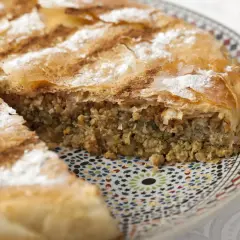 Une part de pastilla espagnol, feuilletée et saupoudrée de sucre glace et de cannelle, repose sur une assiette décorée.