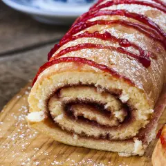 Un délicieux roulé à la confiture, saupoudré de sucre glace et décoré d'un coulis rouge vif, prêt à être dégusté.