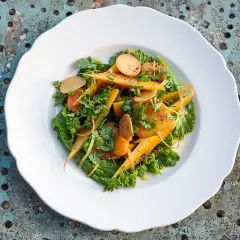 Salade colorée de carottes confites, parsemée d'herbes fraîches et de fines lamelles de radis, sur une assiette blanche.