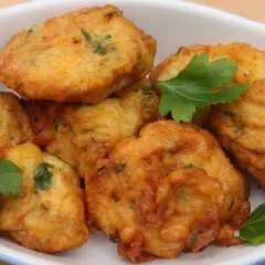Des beignets dorés et croustillants, comme les farinettes de grand-mère, garnis d'herbes fraîches, dans un plat blanc.