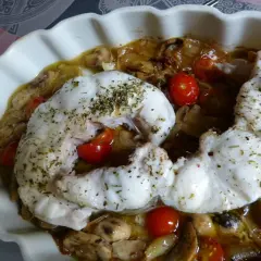 Filet de congre au four, tendre et savoureux, servi avec des tomates cerises et des champignons dans un plat blanc.