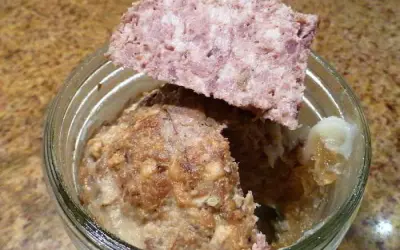 Un bocal de marmiton pâté de sanglier en bocaux stérilisés, avec une tranche de pâté posée sur le bord.