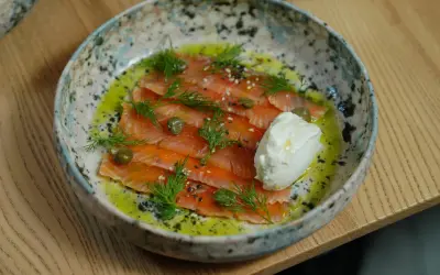 Saumon gravlax maison, fines tranches de poisson cru mariné, garnies d'aneth, de câpres et d'une quenelle de crème fraîche.