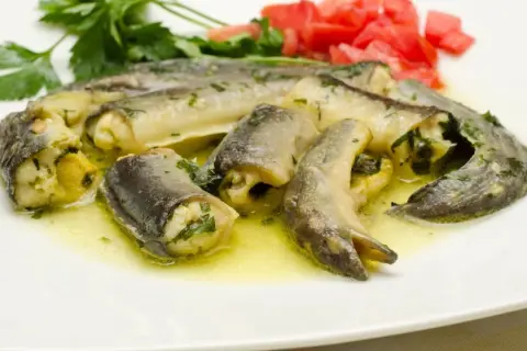 Délicieux morceaux d'anguille roulée, baignant dans une sauce dorée, parfaits pour apprendre comment préparer une anguille. Garniture de persil et tomates.