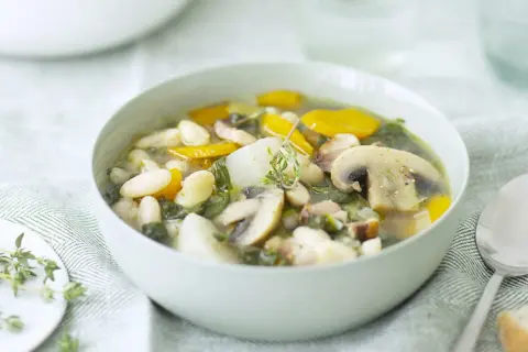 Un bol de soupe haricots blancs réconfortante avec des champignons, des carottes et des herbes fraîches.