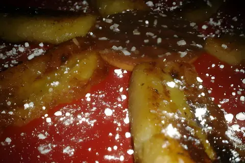 Délicieuse banane grillée à la poêle, saupoudrée de sucre glace, sur une assiette rouge. Un dessert gourmand et simple.