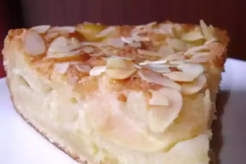 Une part de gâteau d'Ève, aux pommes et amandes effilées, dorée et appétissante.
