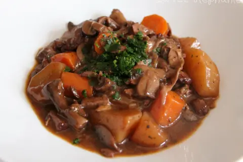 Un savoureux bourguignon végétarien avec des champignons, des carottes et des pommes de terre, garni de persil frais.